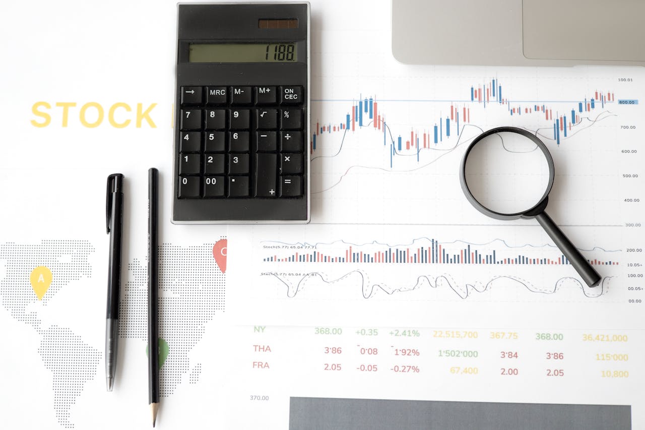 Flat lay of stock market analysis tools including calculator, graphs, and magnifying glass.